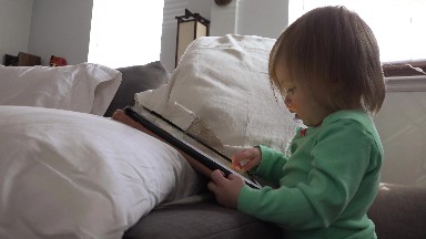 Toddler tablet computing closeup with bright window light background.