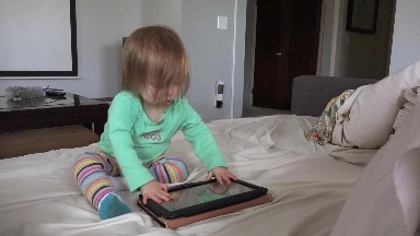Toddler tablet computing in living room seated on white day bed.