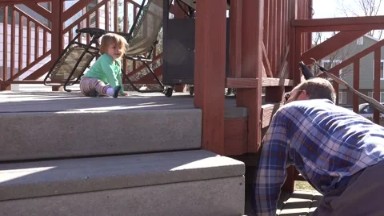 Dad playing peek-a-boo hiding game with bay on sunny outdoor deck.