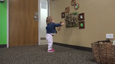 Toddler in jean jacket touching 3D elephant wall hanging art painting.