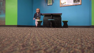 Toddler walking from kids table across carpet floor to camera.
