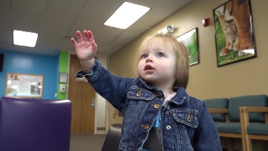 Toddler in jean jacket reaching at pediatrics doctors office waiting room.