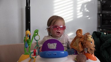 Toddler bouncing in seated toy with rose colored glasses in baby einstein.