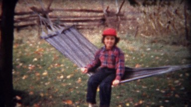 1944: Girl rocking on hammock hanging in autumn fall leaves.