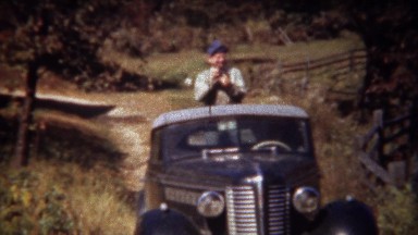 1946: Man filming riding on top of classic 40s Lincoln car at farm.