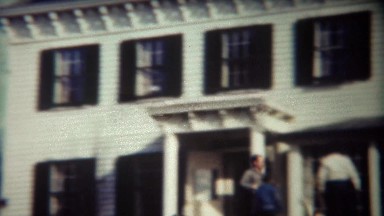 1947: Man running past white mansion house throwing stick for dog.