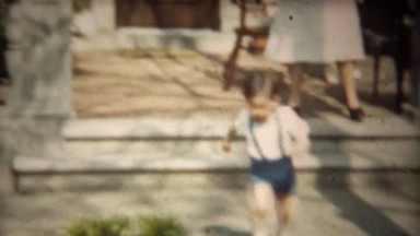 1942: Toddler boy running in blue suspenders from home porch closeup.