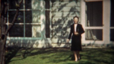 1942: Women in black skirt suit walking from home in spring blossoms.