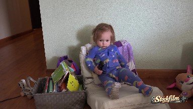 Toddler Lounging Back in Small Chair with TV Remote Control. Denver, Colorado
