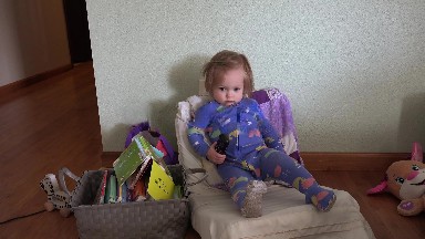 Toddler lounging back in small chair with tv remote control. DENVER, COLORADO