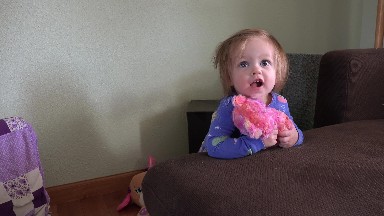Toddler hugs pink stuffed animal bear toy on brown family couch. DENVER,