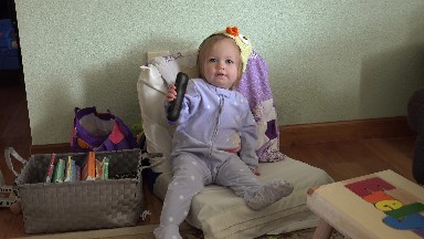 Baby in duck hat sitting on small chair tv remote playing with tongue. DENVER,
