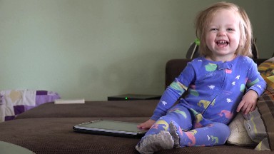 Laughing baby playing with tablet computer on brown couch. DENVER, COLORADO