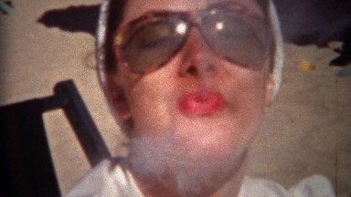 1944: Sunglasses woman smoking cigarette at the beach smiling big. TRYON, NC