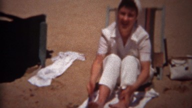 1944: Woman shaking out beach sand from feet seated on canvas chair. TRYON, NC