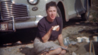 1943: Family enjoys impromptu roadside lunch picnic as classic car drives by.