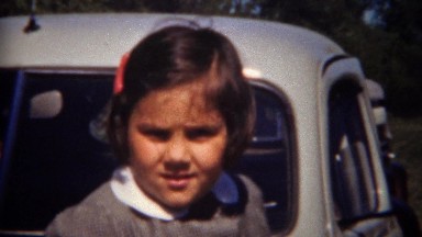 1944: Cute child in grey schoolgirl uniform outdoor gray classic car leaning.