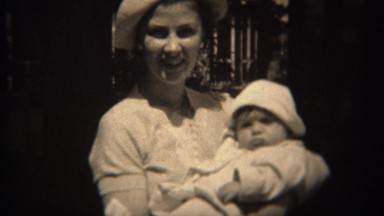 1937: Mother in white fashion hat holding baby daughter in matching outfit.