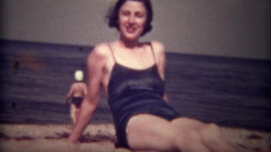 1939: Women in Blue Bathing Suit Chews Gum, Winks, and Smiles on Beach in Tryon, NC