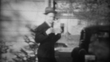 1939: Man Holding Sign with Pipe in Mouth Walks Past Classic Car in Tryon, NC