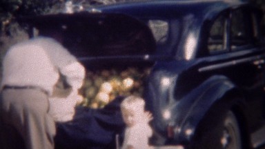 1947: Man packing car truck with orange fruit filling it up.
