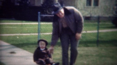 1947: Dad pulling boy in red wagon on suburban sidewalk.
