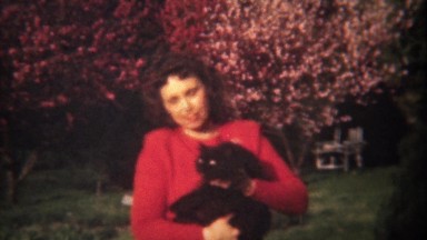 1948: Lady in red petting black cat spring flowering tree blossoms.