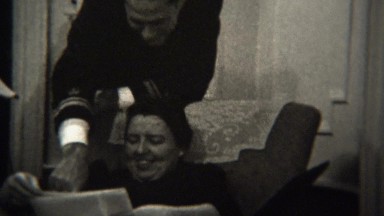 1947: Proud man showing women family photos in living room.