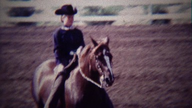 1967: Girl horse riding competition rider trotting around track.
