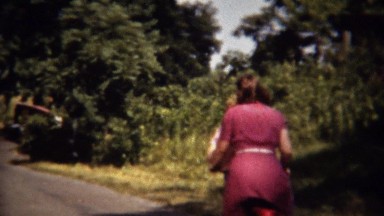 1962: Women bike riding wooded country road sunny day.