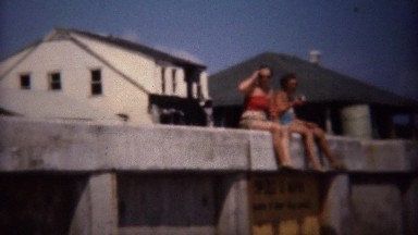 1949: Women Sitting on Pier Overlooking Sunny Ocean Beach Waves.