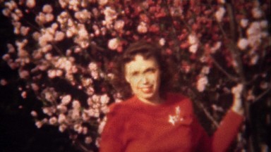 1949: Lady in red posing at pink spring flowering tree blossoms.