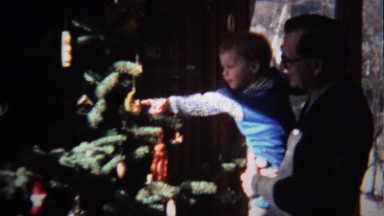1972: Toddler touching Christmas tree ornament in dad's arms.