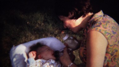 1971: Women feeding baby milk bottle hippie gypsy colorful.