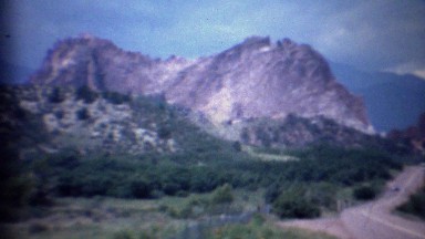 1963: Cars driving past scenic mountain rock formation gap.