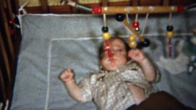 1958: Baby Plays Wooden Mobile Rings Above Crib Bed.