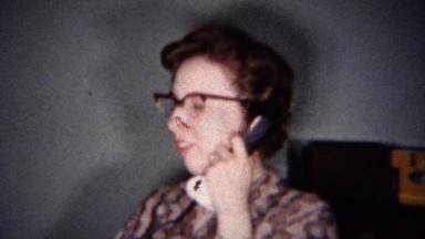 1959: 1950s Woman in Paisley Shirt and Eyeglasses Talking on Rotary Phone