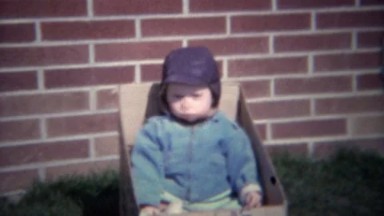 1961: Bundled sick baby sneezes in outdoor cardboard box.