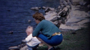 1962: Mother baby enjoy lakeshore water summer rock throwing.