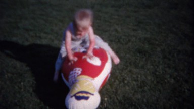 1962: Baby wrestles inflatable clown toy in playground backyard.