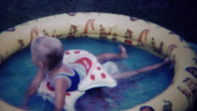 1963: Girl cools down on hot summer day in backyard kiddie pool.