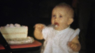 1963: Blonde baby girl eating half birthday cake with spoon.