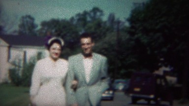 1964: Italian married couple walking sidewalk street sunny day.