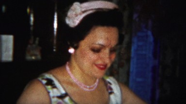 1964: Italian American women folding white linen sheets flower dress.