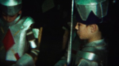 1964: Young soldier knights boy tapping shoulder fake sword blade.
