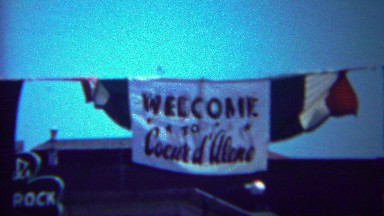 1954: Welcome Coeur d'Alene Flag Sign Hanging Above Main Street.