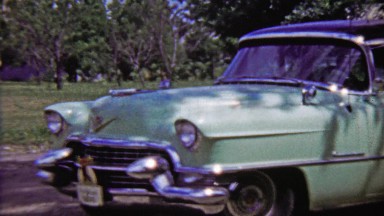 1959: Teal Cadillac 4 door classic car parked in outdoor green space.