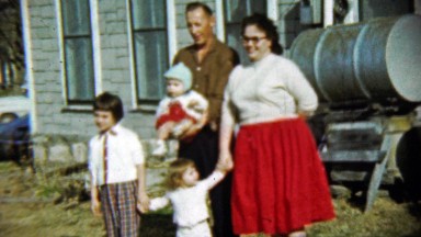 1959: Happy family poses gasoline fuel barrell front house.