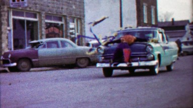 1959: Mannequin strapped to decorated parade car hood.