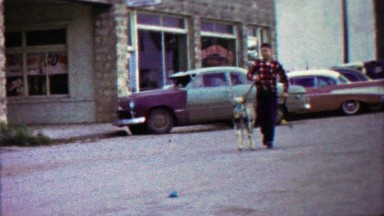 1959: Boy walking leashed parade goat down mainstreet downtown.